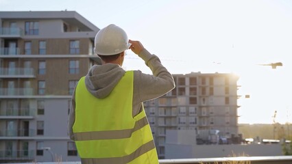 Man constructive engineer with white hard hat and safety vest is using a tablet computer while...