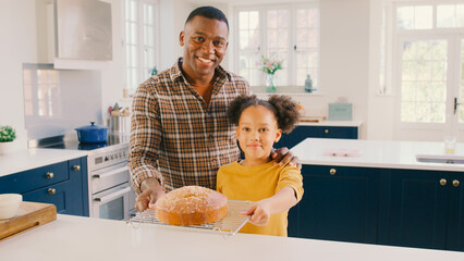 Portrait Of Proud Father And Daughter At Home In Kitchen With Homemade Cake They Have Baked Together