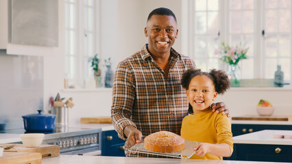 Portrait Of Proud Father And Daughter At Home In Kitchen With Homemade Cake They Have Baked Together
