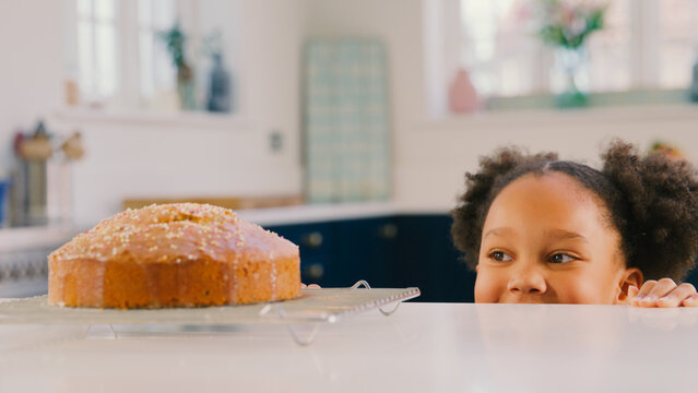 Hungry Girl At Home In Kitchen Looking At Homemade Cake With Sprinkles On Counter
