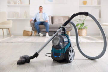 Man resting on sofa at home, focus on vacuum cleaner