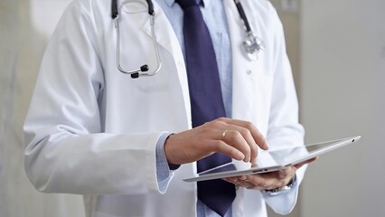 Doctor man wearing lab coat and stethoscope using tablet computer in hospital. Medicine and science