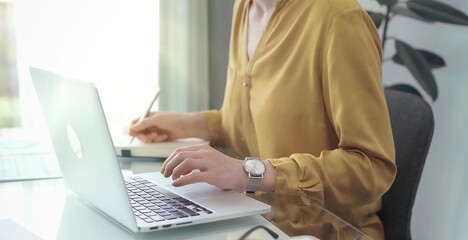 Naklejka premium Unrecognizable professional woman is making notes and working with laptop in modern office. Yellow blouse is passing to adult businesswoman. Business concept