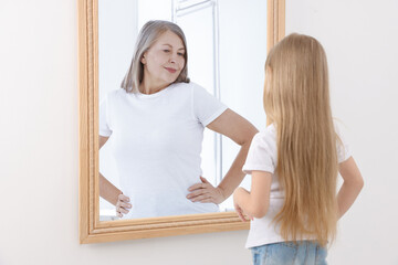 Little girl seeing herself as senior woman in mirror. Conceptual collage about past and future,...