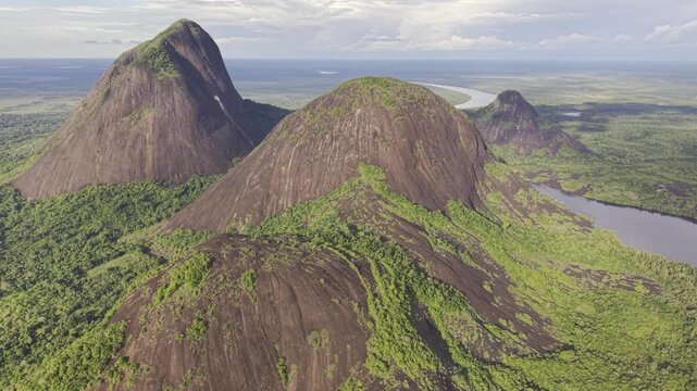 Aerial view of the striking Cerros de Mavicure, where imposing dark rock formations meet the lush green rainforest and winding rivers, Cerros Mavicure, Colombia.