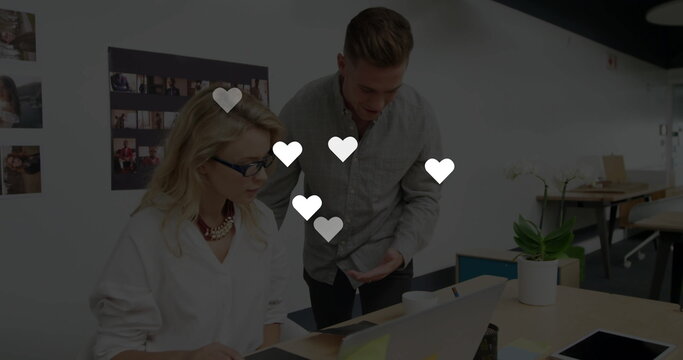 Reviewing coworkers wearing glasses typing on laptop in open-plan office, with orchid plant