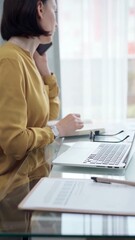 Young professional woman is talking by smartphone in modern office. Yellow blouse is passing to adult businesswoman. Business people concept