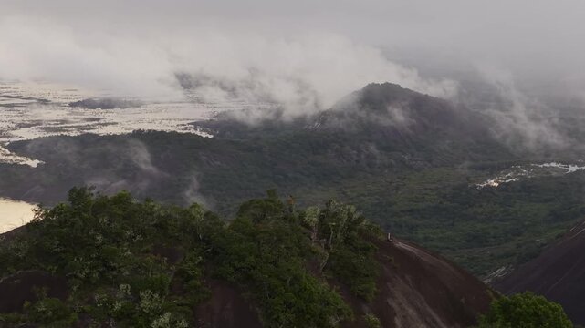 Aerial view of the landscape with lush green trees, rivers, and low-lying clouds creating a serene, dreamy atmosphere, Cerros Mavicure, Colombia.