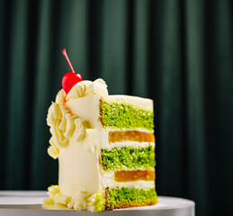 Delicious green layer cake with cherry on top presented on a white pedestal