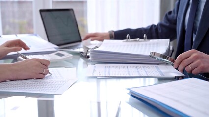 Business people wearing blue suits are reviewing financial data in office. Two professionals analyzing paper reports using calculators. Audit and taxes concept