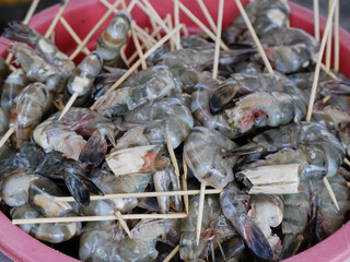Fresh raw shrimp skewers arranged in a red container, ready for grilling or cooking, seafood preparation concept, closeup detail of uncooked prawns on wooden sticks for culinary use.