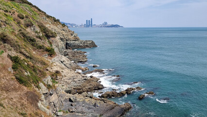 
 Rocky coastline with cliffs and sparse vegetation, turquoise sea with small waves crashing...