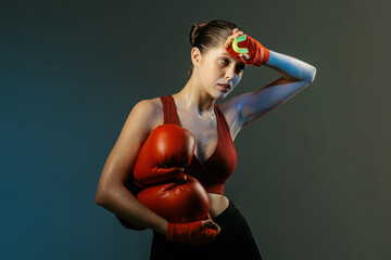 Sweaty female boxer with red gloves holding mouthguard after training on dark background