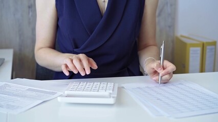 Businesswoman with dark blue dress is using white calculator and taking notes in her office. Taxes and audit in business