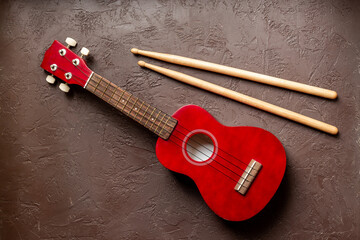 Red small guitar ukulele with drumsticks. Musical instruments, top view