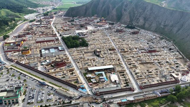 Aerial view of the extensive Labrang Monastery complex, a tapestry of buildings nestled against a backdrop of majestic mountains, Labrang Monastery, Gansu, China.