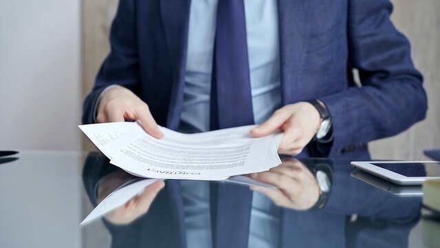 Businessman reviewing documents at office desk. Close-up of a professional man's hands examining paperwork with pen and tablet in sight. Business people concept