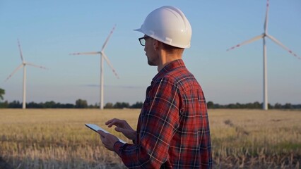 Man engineer at work is wearing a white protective helmet and taking notes with a tablet computer...
