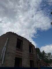 Abandoned partially demolished brick building beneath dramatic cloudy sky, rubble and empty window...