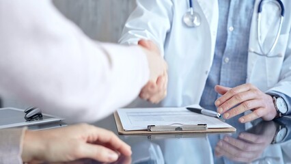Doctor and patient handshake in clinic setting above the glass table. Medicine concept trust and...