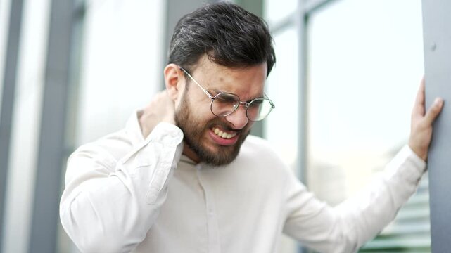 Tired businessman suffering from neck pain while standing on the street near a modern office building. Upset male worker feels pain, discomfort, spasms, massages and rubs sore muscles. Close up