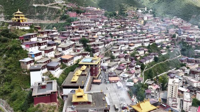 Aerial view of the Larung Gar Buddhist Academy, a sprawling tapestry of red-roofed dwellings clinging to the verdant slopes, Garz&ecirc;, Sichuan, China.