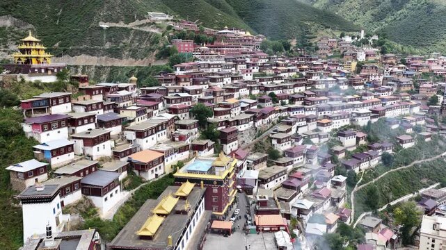 Aerial view of Larung Gar's clustered red-roofed dwellings nestled amid rolling green hills, creating a striking contrast of human settlement and natural beauty, China.