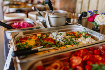 Buffet table with assorted cheeses, herbs, and fresh greens in a stainless steel tray, ready to...