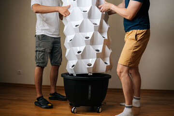 Cropped shot of two urban farmers placing main body of vertical hydroponic tower garden onto its...