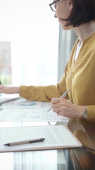 Adult professional woman is working with laptop in flair office. Yellow blouse is passing to adult...