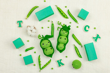 Handmade crochet pea pods and fresh green peas on a natural fabric background, with toy vegetables