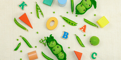 Handmade crochet pea pods and fresh green peas on a natural fabric background, with toy vegetables