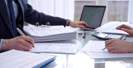Obraz premium Business people wearing blue suits are reviewing financial data in office. Two professionals analyzing paper reports using calculators. Audit and taxes concept