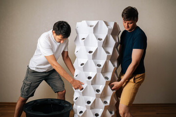 Two men positioning main body of vertical hydroponic tower garden onto its base, working together...