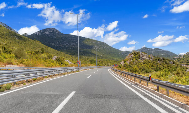 A winding mountain highway with a 90 km h speed limit sign stretches under a bright blue sky with scattered clouds.