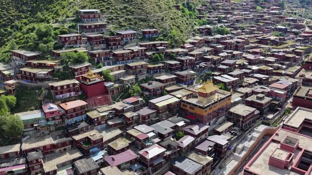 Aerial view of the Dege Parkhang Printing house, a symphony of red-roofed buildings cascading down the verdant slopes of Sichuan, China, Dege, Sichuan, China.