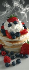 Stacked pancakes topped with whipped cream, strawberries, and blueberries, with steam rising
