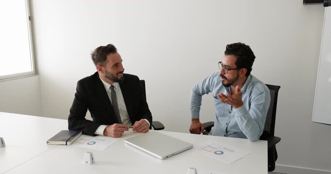 Two positive diverse male business colleagues discussing marketing research result, financial investment strategy, teamwork, talking at meeting table. Business professional man consulting expert