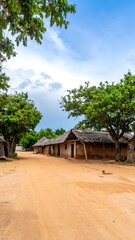 Sandy road leads past simple, thatched-roof dwellings under a partly cloudy sky