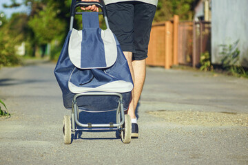 Man walking to market with blue grocery trolley on sunny day. Convenient grocery shopping solution for elderly seniors. Concept of slow living, mindful consumption and modern sustainable shopping