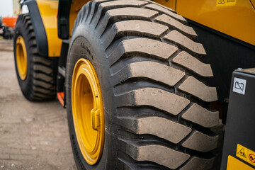 Large heavy machinery tire close-up with rugged tread and bright yellow rim, construction equipment wheel detail, industrial vehicle, loader, excavator, bulldozer