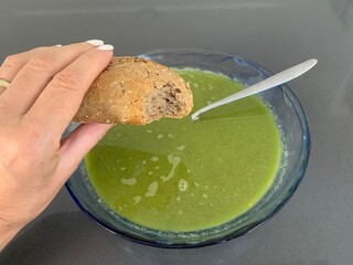 Woman holding a half eaten bread roll above a plate of homemade pea soup