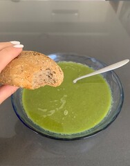 Woman holding a half eaten bread roll above a plate of homemade pea soup