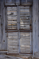 Weathered Wooden Shutters on Old House. A vertical close-up of aged, gray wooden shutters on an old building, showing rustic texture, cracks, and weathered details against a wood plank wall.
