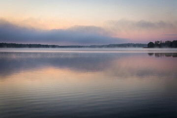 Fototapeta premium Serene dawn landscape of a calm lake with misty fog reflecting colorful skies