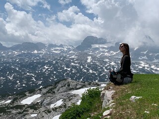 Young woman meditating in a lotus position on a mountain top with a breathtaking snowy landscape
