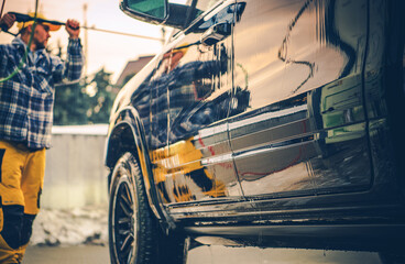 Man Pressure Washing a Black SUV During Golden Hour at a Car Detailing Location