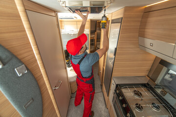 RV Worker Repairs Overhead Unit in Modern Travel Trailer Kitchen