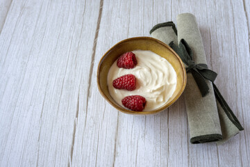 Green ceramic bowl and natural yogurt with red berries on the white wood table.