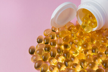 Omega capsules with fish oil with white bottle on pink background.